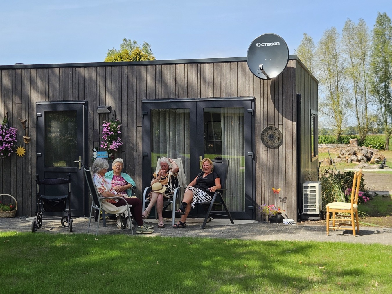 Bewoners van De Vrijheid met oprichtster Marga van Overvelden zitten voor een luxe zorgunit van Boxtom.