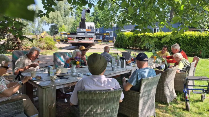 Bewoners van De Vrijheid zitten buiten aan de koffie en taart terwijl de zorgwoning van Boxtom wordt geplaatst