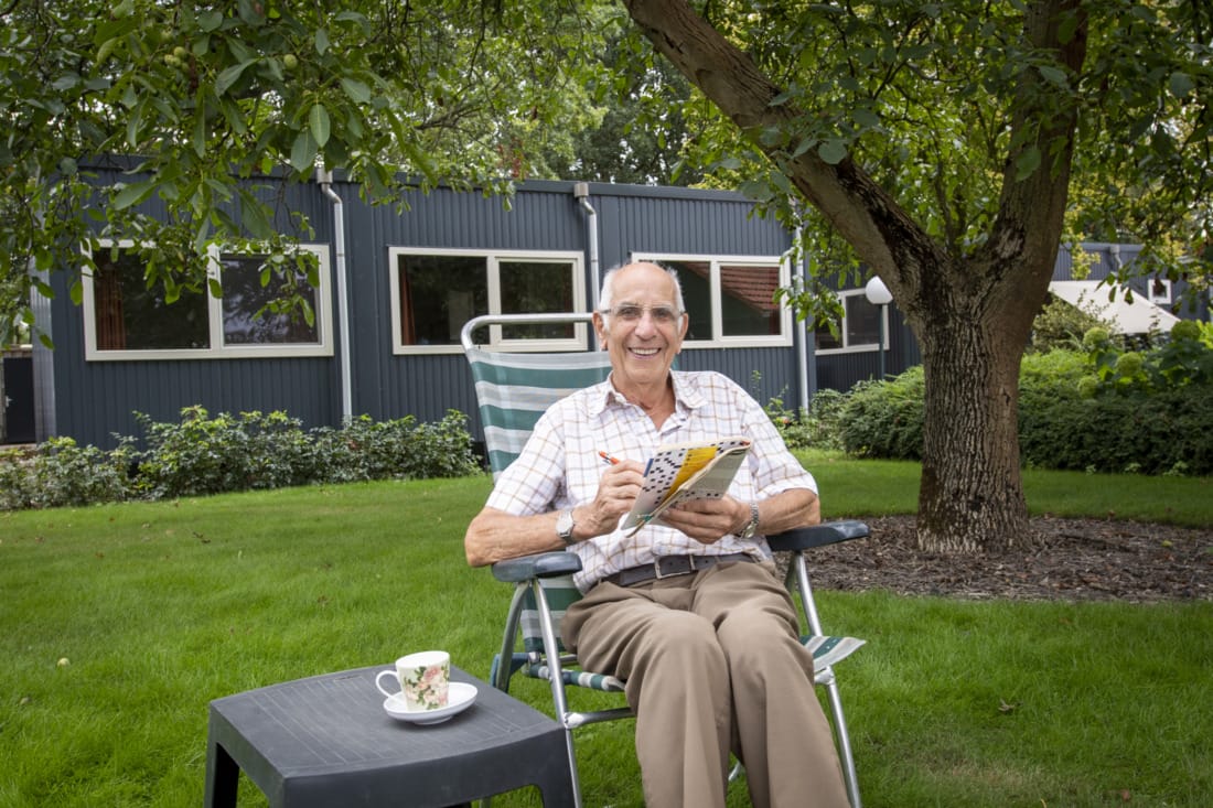 Bewoner zit voor mantelzorgwoning thee te drinken.